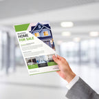 A HAND IN A GRAY SUIT HOLDS A PRINTED REAL ESTATE BROCHURE FEATURING A HOUSE PHOTO AND GREEN-AND-WHITE DESIGN IN A MODERN OFFICE SETTING.