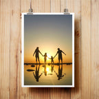 FAMILY SILHOUETTE ART PRINT FEATURING A FAMILY HOLDING HANDS IN SHALLOW WATER AT SUNSET, DISPLAYED ON A LIGHT WOOD WALL WITH METAL CLIPS.