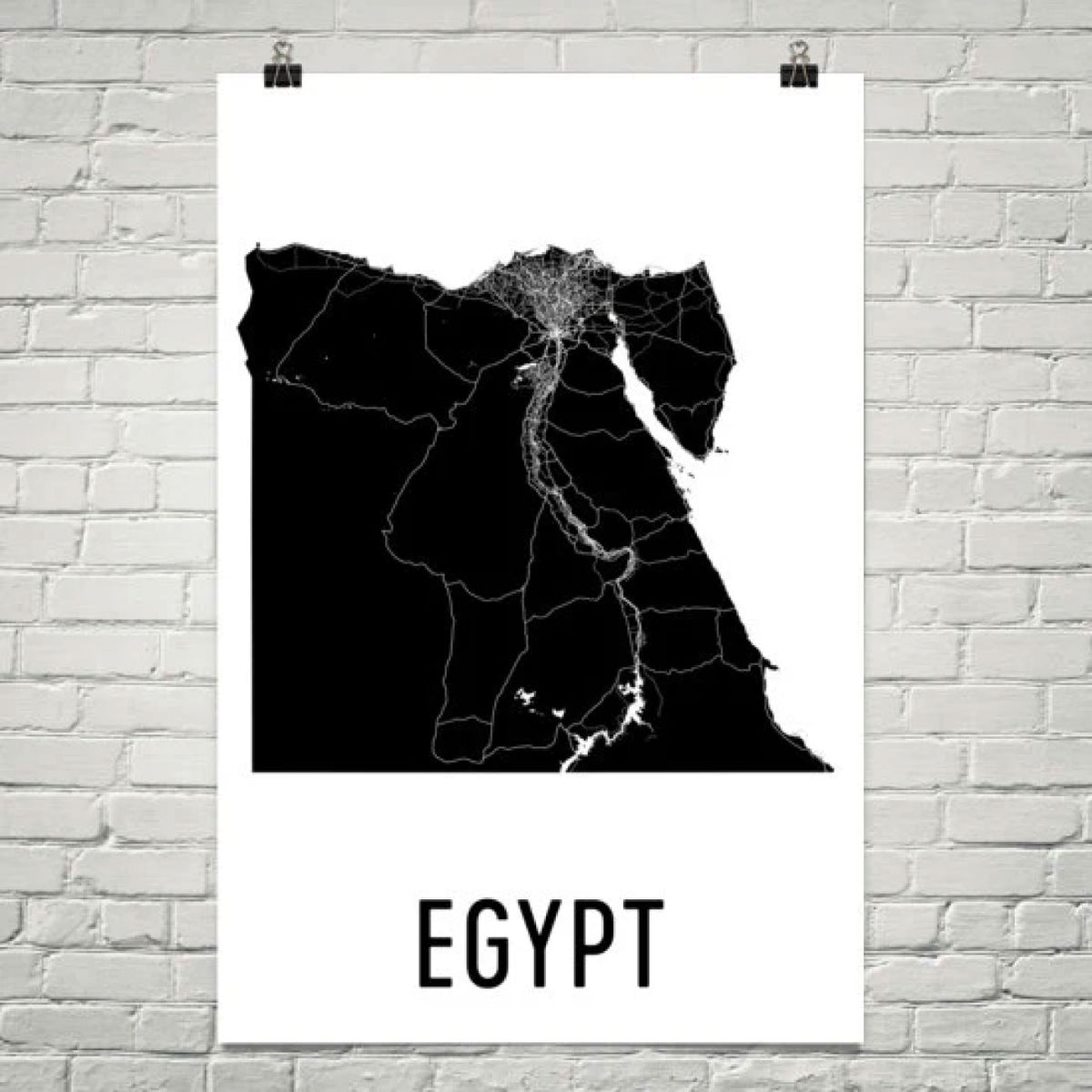 MINIMALIST EGYPT MAP POSTER FEATURING A BLACK SILHOUETTE MAP WITH ROADS AND THE NILE RIVER, DISPLAYED ON A WHITE BRICK WALL.