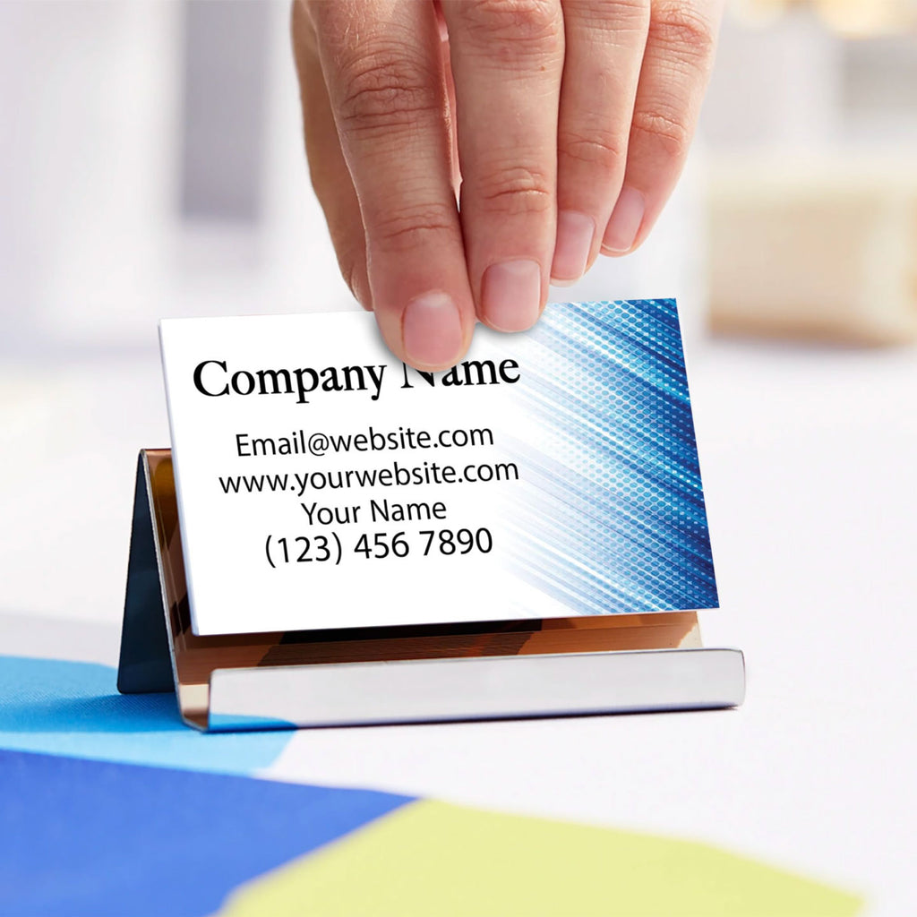 CUSTOM PRINTED BUSINESS CARD WITH BLUE GRAPHICS AND CONTACT INFORMATION BEING PLACED INTO A METAL BUSINESS CARD HOLDER ON A DESK.