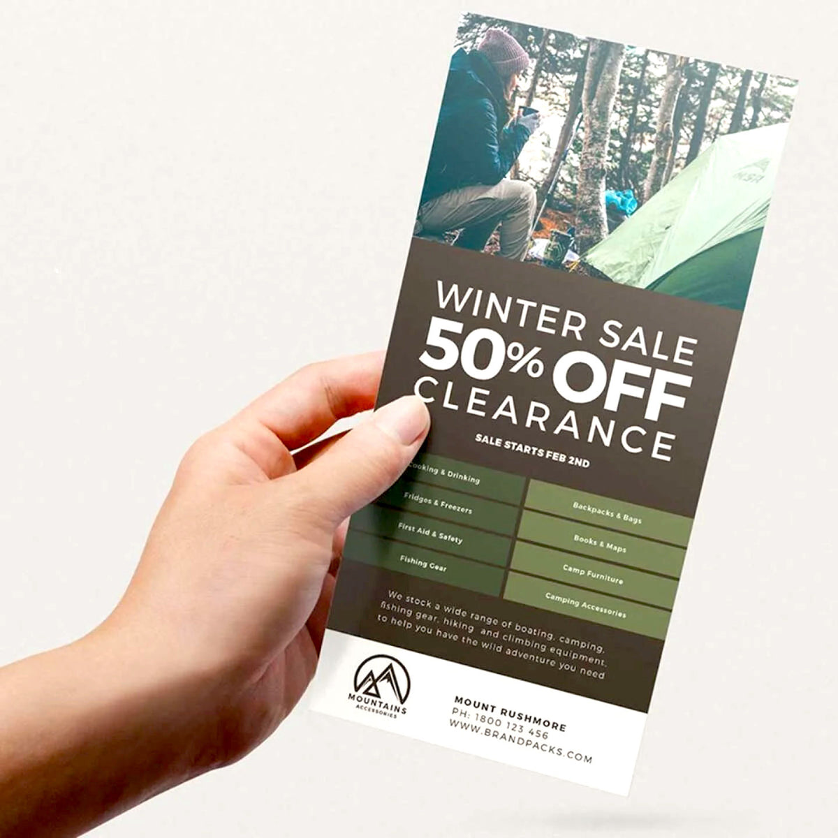 HAND HOLDING A CUSTOM PRINTED PROMOTIONAL POSTCARD FEATURING A WINTER CLEARANCE SALE AND OUTDOOR CAMPING DESIGN ON A CLEAN WHITE BACKGROUND.