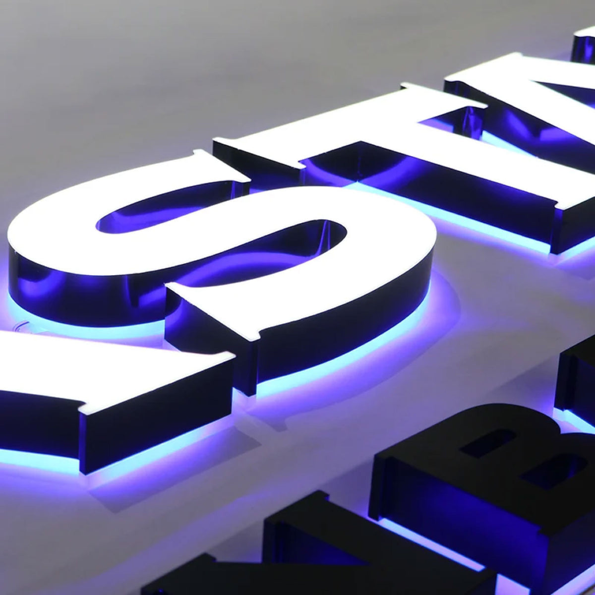 3D ILLUMINATED LETTERS WITH WHITE FACES, BLACK RETURNS, AND BLUE-PURPLE LED HALO LIGHTING, DISPLAYED ON A LIGHT GRAY BACKGROUND.