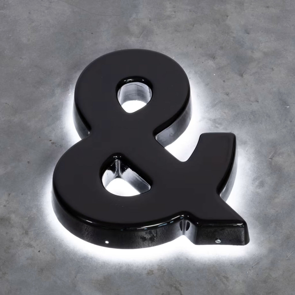 GLOSSY BLACK 3D AMPERSAND SIGN WITH WHITE LED HALO BACKLIGHTING, MOUNTED ON A TEXTURED GRAY CONCRETE WALL.