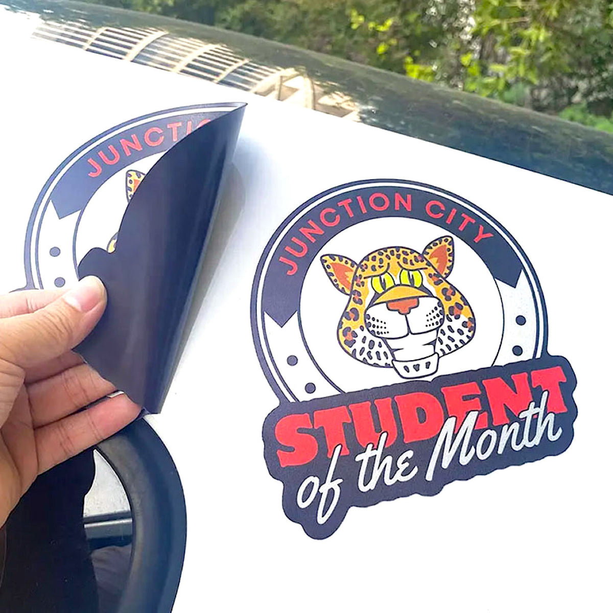 CUSTOM PRINTED CONTOUR-CUT MAGNETIC SIGN FEATURING JUNCTION CITY STUDENT OF THE MONTH GRAPHICS WITH A LEOPARD MASCOT, SHOWN APPLIED TO A WHITE VEHICLE WITH THE FLEXIBLE MAGNETIC MATERIAL PARTIALLY LIFTED.