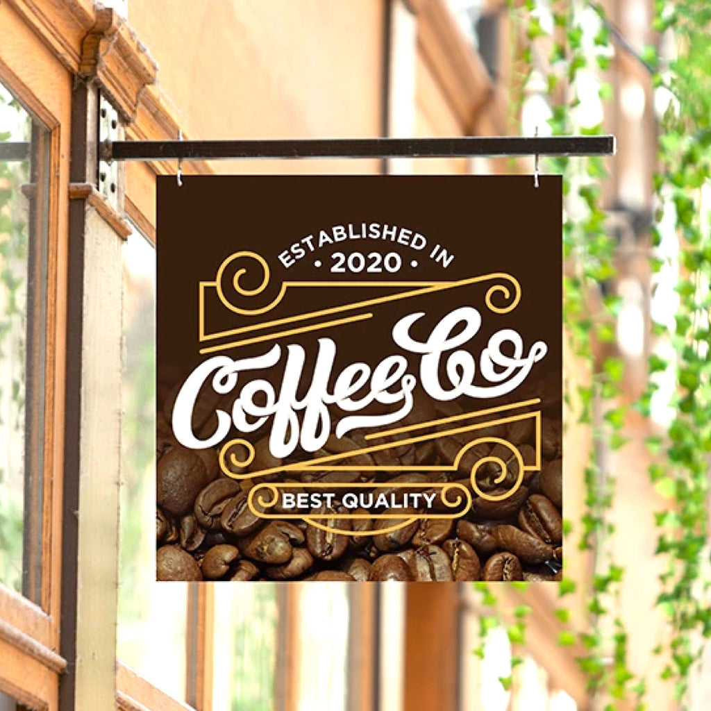 CUSTOM PRINTED ALUMINUM COFFEE SHOP SIGN FEATURING COFFEE & CO BRANDING WITH WHITE AND GOLD GRAPHICS AND COFFEE BEANS, HANGING FROM A BLACK METAL BRACKET OUTSIDE A STOREFRONT.