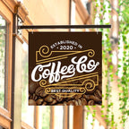 CUSTOM PRINTED ALUMINUM COFFEE SHOP SIGN FEATURING COFFEE & CO BRANDING WITH WHITE AND GOLD GRAPHICS AND COFFEE BEANS, HANGING FROM A BLACK METAL BRACKET OUTSIDE A STOREFRONT.