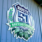 CUSTOM PRINTED ALUMINUM SIGN FEATURING ROUTE 51 BREWING COMPANY BRANDING WITH A SHIELD, WHEAT, HOPS, AND GREEN BANNER GRAPHICS, MOUNTED ON A BLUE CORRUGATED METAL EXTERIOR WALL.