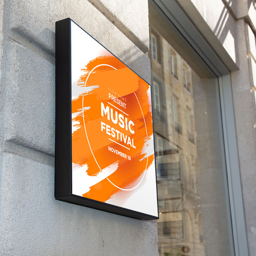 CUSTOM PRINTED TRANSLUCENT BACKLIT SIGN INSERT FEATURING A BOLD ORANGE AND WHITE PRESENT MUSIC FESTIVAL POSTER, DISPLAYED IN A FRAMED SIGN MOUNTED ON A GRAY STONE WALL.
