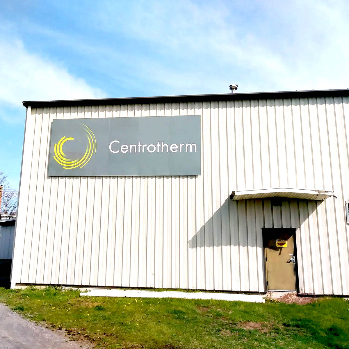 CUSTOM PRINTED ACM BUILDING SIGN FEATURING CENTROTHERM BRANDING WITH A GRAY BACKGROUND AND YELLOW LOGO, MOUNTED ON THE EXTERIOR OF A WHITE INDUSTRIAL BUILDING.